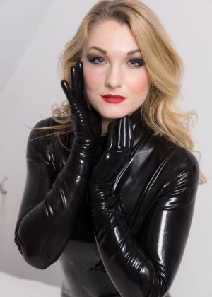 Красивая блондинка украшает свое обнаженное тело в латексном комбинезоне с перчатками и каблуками